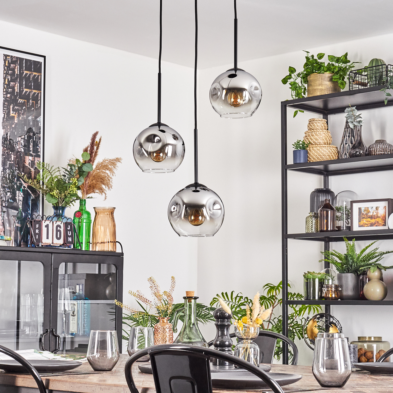 Esszimmer mit Hängelampen, Regalen mit Pflanzen und Dekoration sowie einem gedeckten Tisch.