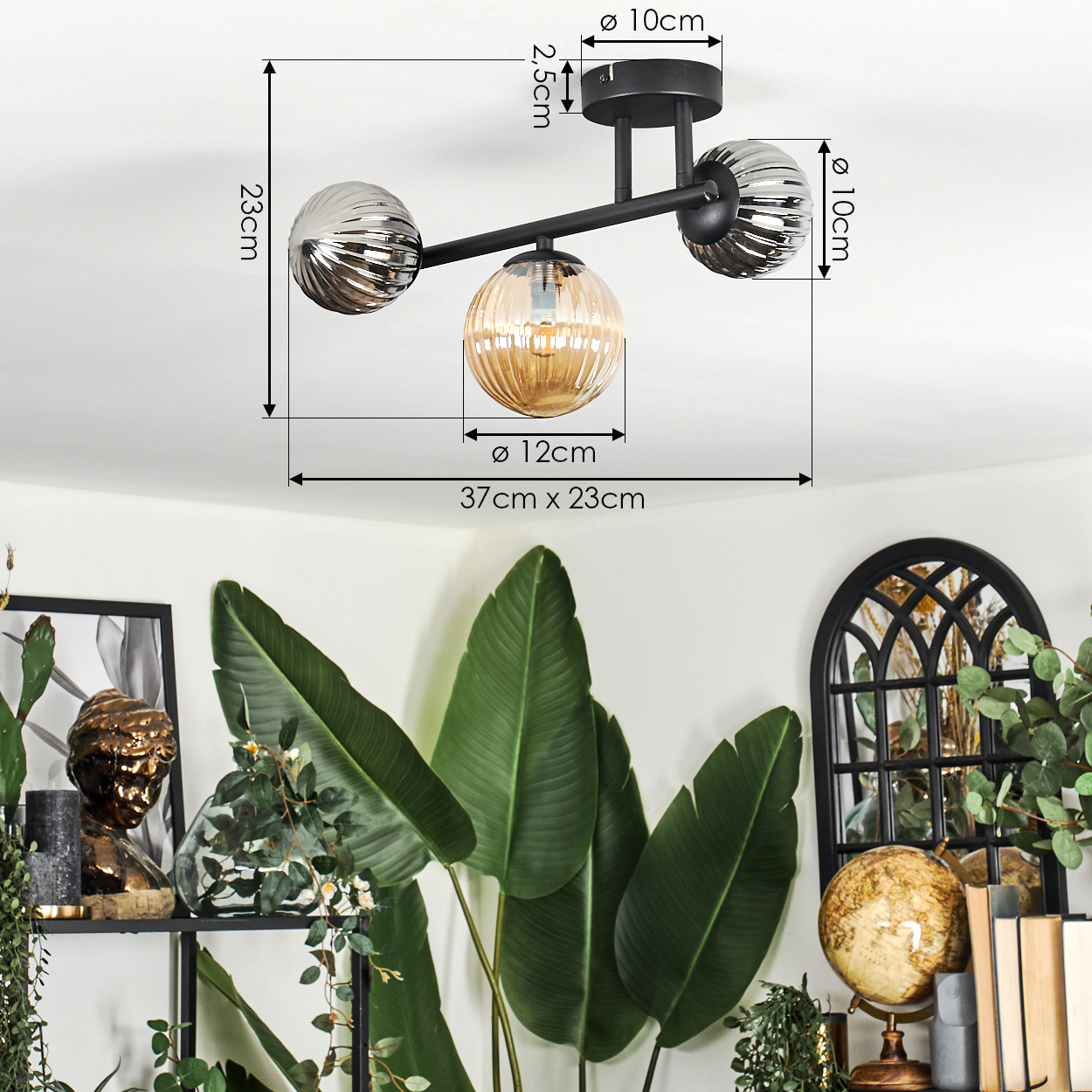 Eine moderne Deckenlampe mit drei Glaskugeln. Darunter große grüne Blätter und Dekorationen auf einem Regal und einem Globus.