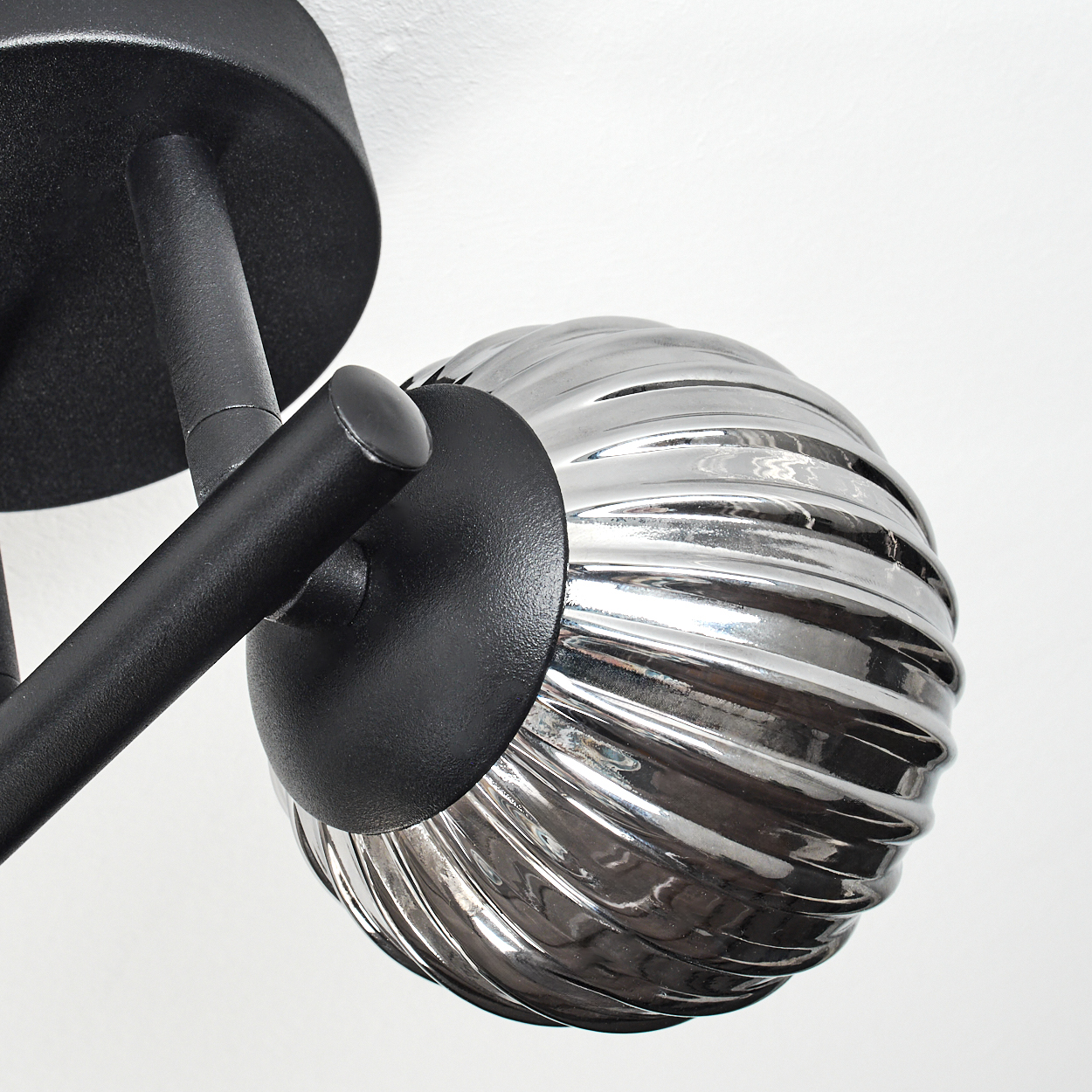 Nahaufnahme einer modernen Lampe. Sie hat einen schwarzen Arm und eine silberne, gerippte Glaskugel auf weißem Hintergrund.
