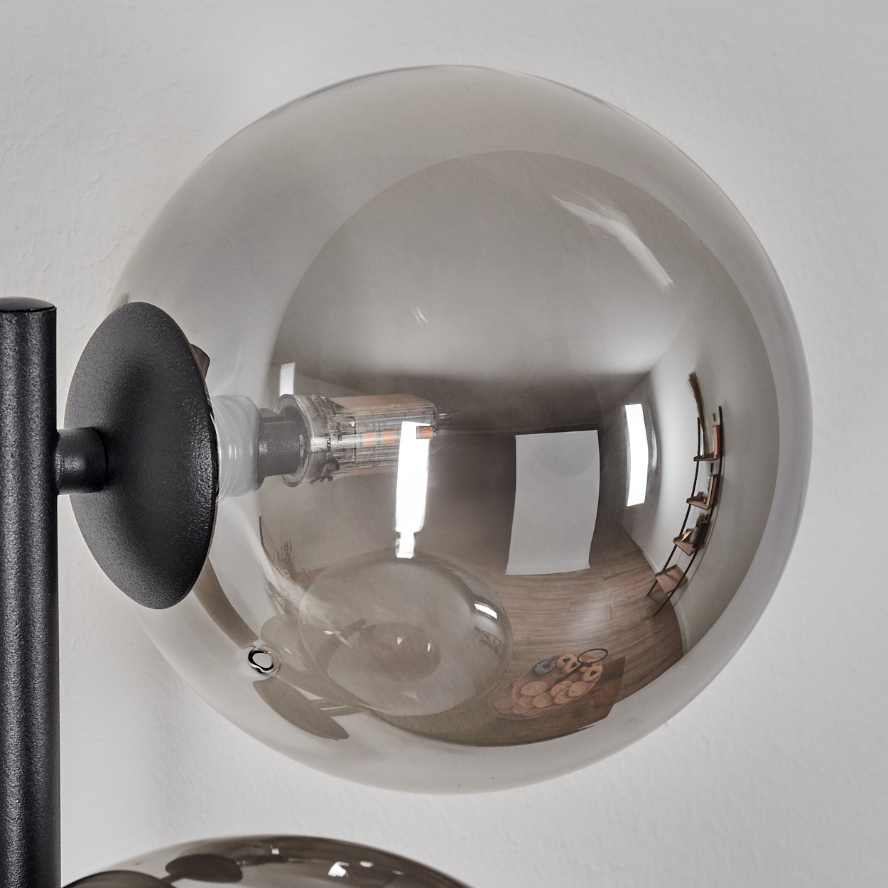 Nahaufnahme einer modernen Lampe. Eine graue Glaskugel spiegelt einen Raum mit Holzboden, Regalen und einem Korb wider.