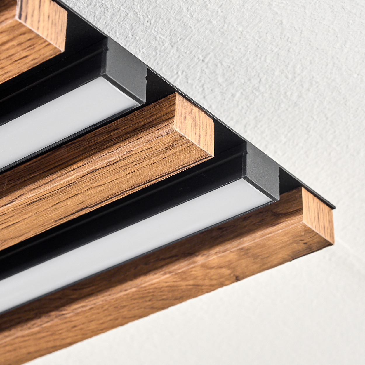 Nahaufnahme einer Deckenleuchte mit Holzbalken und weißen Lichtstreifen vor einer weißen strukturierten Decke.