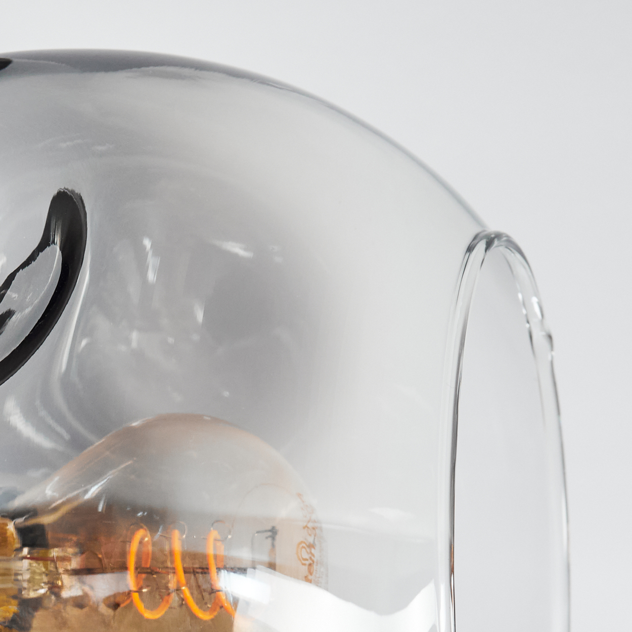 Nahaufnahme eines Glaslampenschirms mit sichtbarer Glühbirne. Das Glas ist klar mit dunklem Akzent. Die Glühbirne leuchtet.