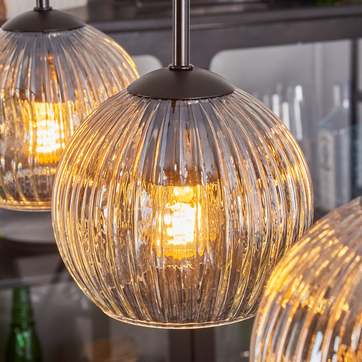 Drei Glas-Pendelleuchten mit strukturierten, gerippten Schirmen sind beleuchtet. Die Leuchten sind von der Decke abgehängt, mit warmem Licht.