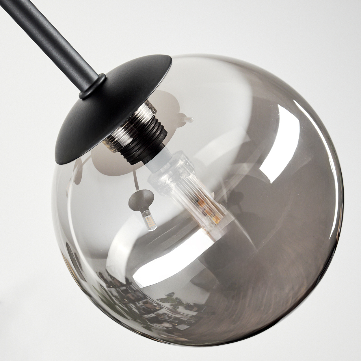 Nahaufnahme einer modernen Lampe. Eine schwarze Metallstange trägt einen rauchigen Glaskolben mit einer Glühbirne. Weißer Hintergrund.