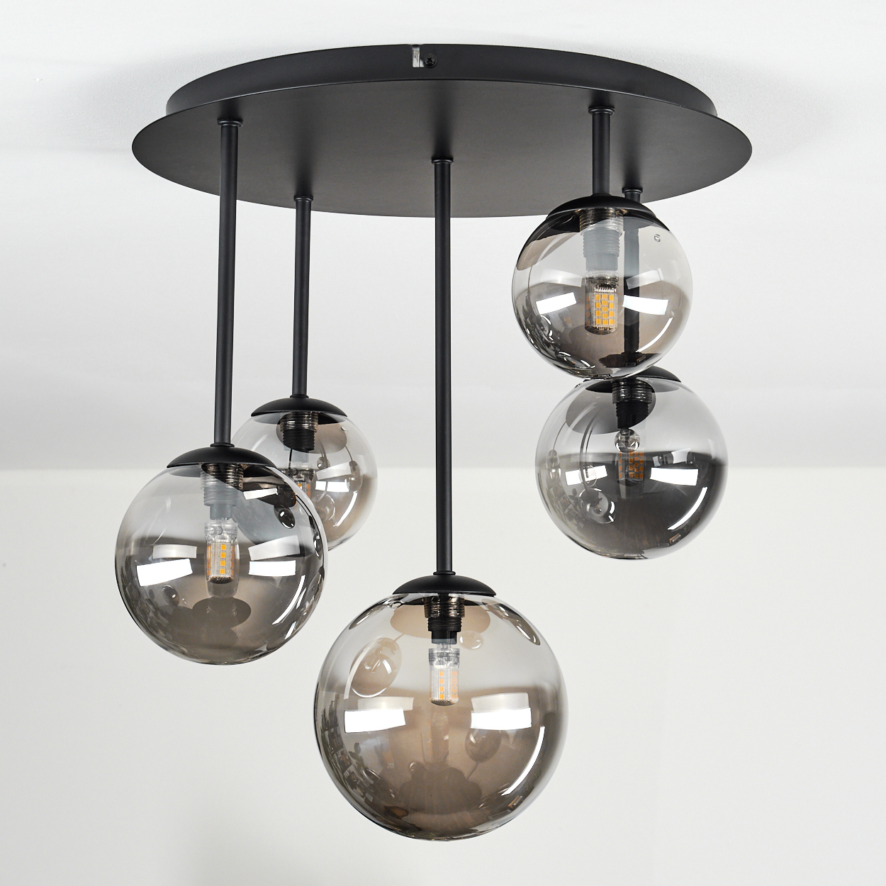 Eine moderne Deckenleuchte mit fünf kugelförmigen Glasschirmen, die von einer schwarzen runden Basis abgehängt sind.