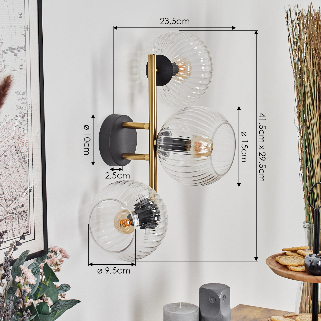 Eine Wandlampe mit drei Glaskugeln. Die Lampe ist gold und schwarz. Maße sind angegeben. Eine Karte und Dekoration sind daneben.