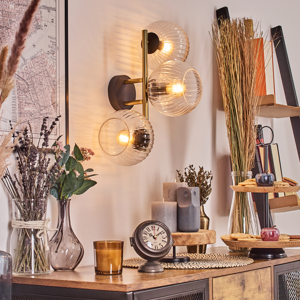 Eine dekorative Szene mit Wandleuchte, Blumen, Kerzen, einer Uhr und einer Karte. Der Stil ist modern mit warmer, einladender Atmosphäre.