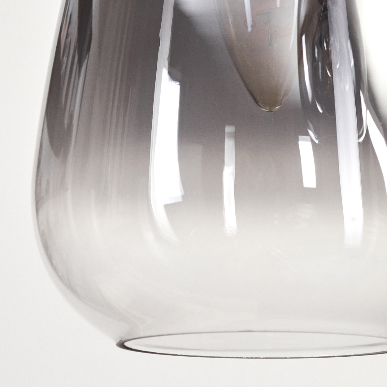 Nahaufnahme eines Lampenschirms aus klarem Glas mit Farbverlauf von Grau zu Transparent. Der Hintergrund ist weiß.