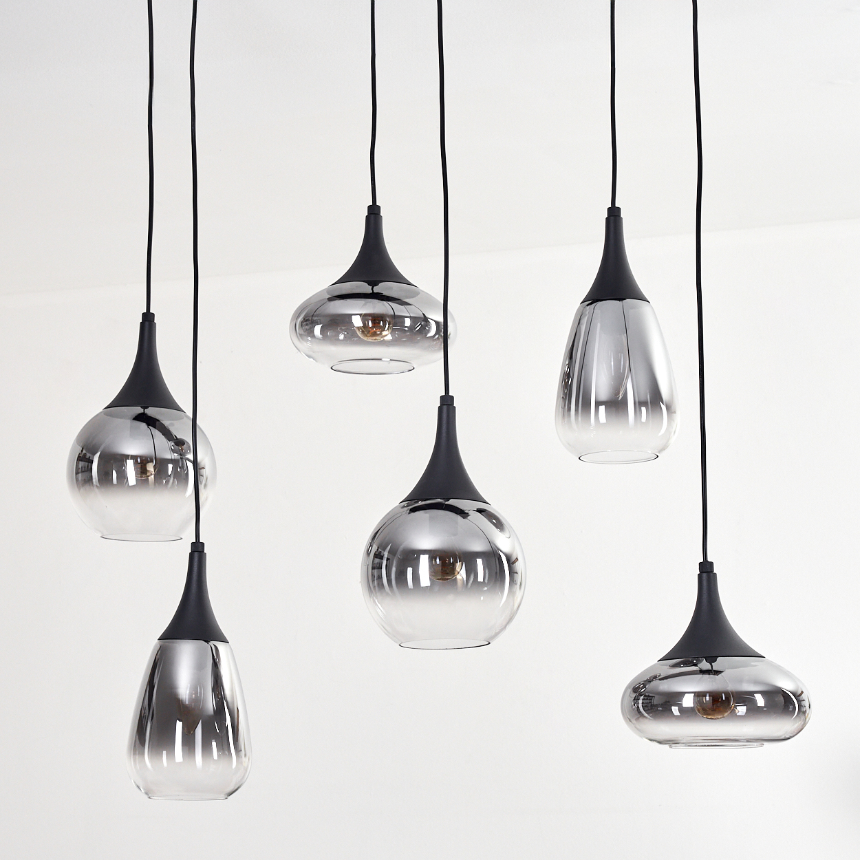 Sechs moderne Pendelleuchten mit reflektierenden Glasschirmen und schwarzen Armaturen hängen vor weißem Hintergrund.