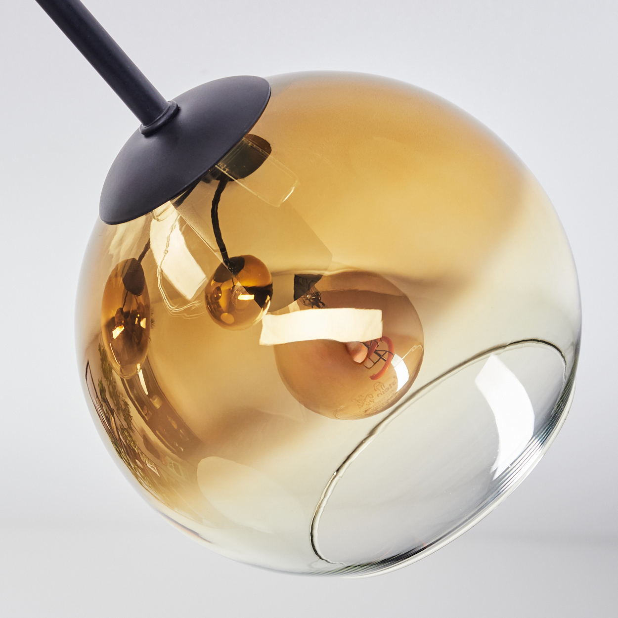 Nahaufnahme einer modernen Leuchte. Sie hat eine große, bernsteinfarbene Glaskugel mit einem schwarzen Metallarm und kleinen Glühbirnen.