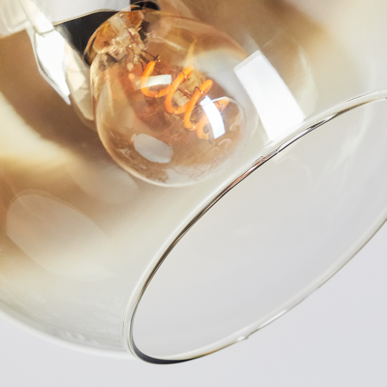 Nahaufnahme einer Glühbirne in einem Glasschirm. Die Glühbirne hat einen orangefarbenen Glühfaden. Der Lampenschirm ist klar und reflektierend.