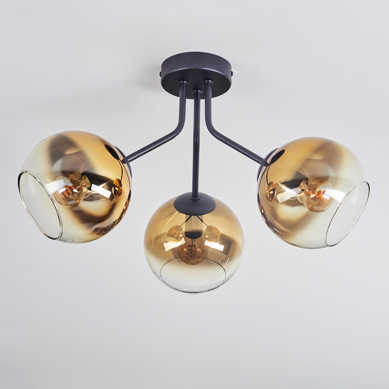 Eine moderne Deckenlampe mit drei kugelförmigen Schirmen. Die Schirme sind bernsteinfarbenes Glas, das die Glühbirnen im Inneren freilegt. Schwarzes Metallgestell.