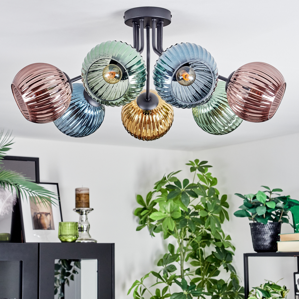 Eine moderne Deckenlampe mit Glasschirmen in verschiedenen Farben, die über Pflanzen und Möbeln in einem Raum hängt.