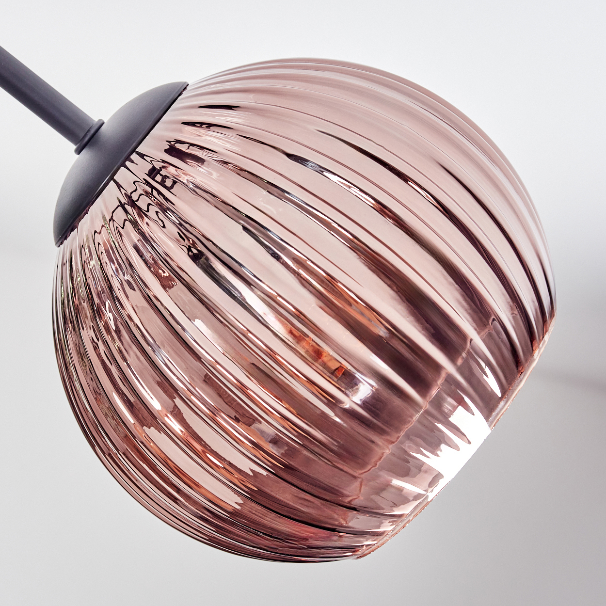 Eine roségoldene Glaskugellampe hängt an einem dunkelgrauen Metallarm vor einem schlichten weißen Hintergrund. Die Kugel hat eine gerippte Textur.