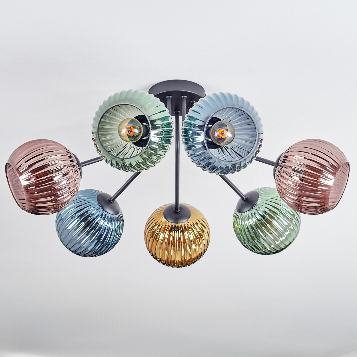Eine moderne Deckenleuchte mit sieben Glasschirmen in verschiedenen Farben: Rosa, Blau, Grün und Gold. Die Leuchte hat ein schwarzes Metallgestell.