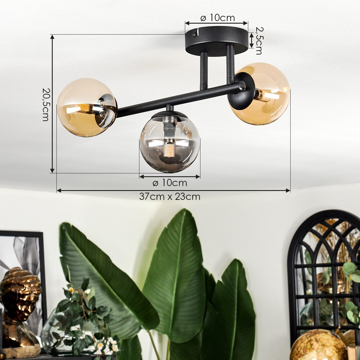Eine moderne schwarze Deckenlampe mit drei Glaskugeln. Im Hintergrund eine Pflanze, eine Büste und ein dekoratives Fenster.