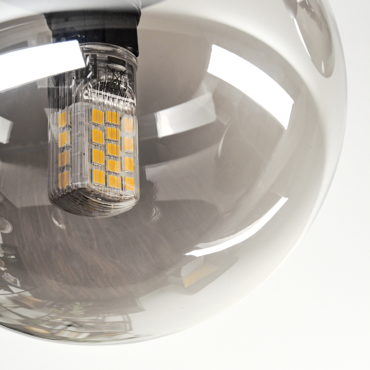 Nahaufnahme einer Leuchte, eine klare Glühbirne mit gelben LEDs, in einem klaren, kugelförmigen Schirm, vor weißem Hintergrund.