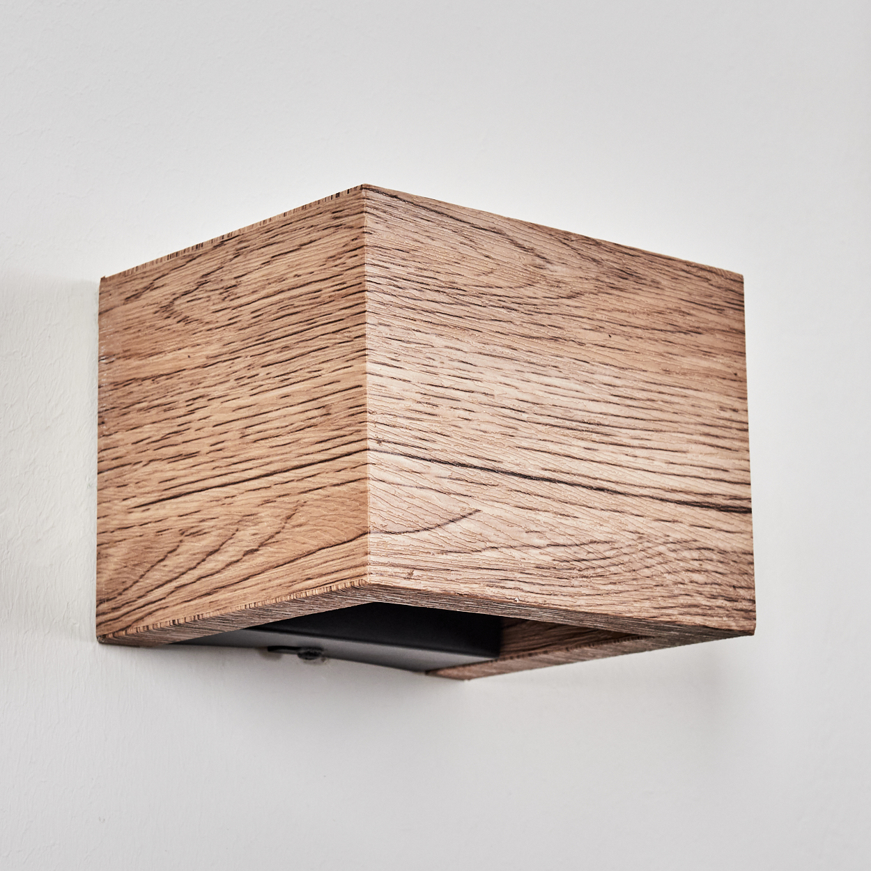 Rechteckige Wandlampe aus Holz mit sichtbarer Holzmaserung, an einer weißen Wand befestigt. Die Lampe hat einen dunklen, vertieften Bereich.