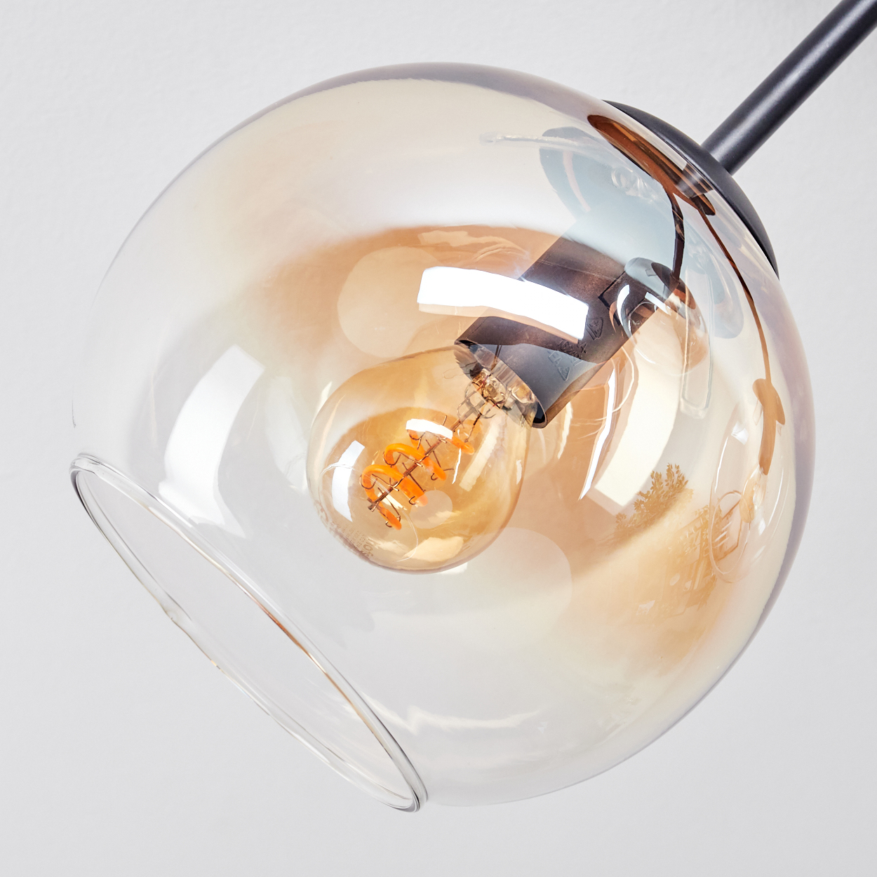 Nahaufnahme einer Glashängeleuchte mit warmfarbiger Glühbirne. Das Glas ist klar mit einem bernsteinfarbenen Farbverlauf. Ein schwarzer Metallstab stützt sie.