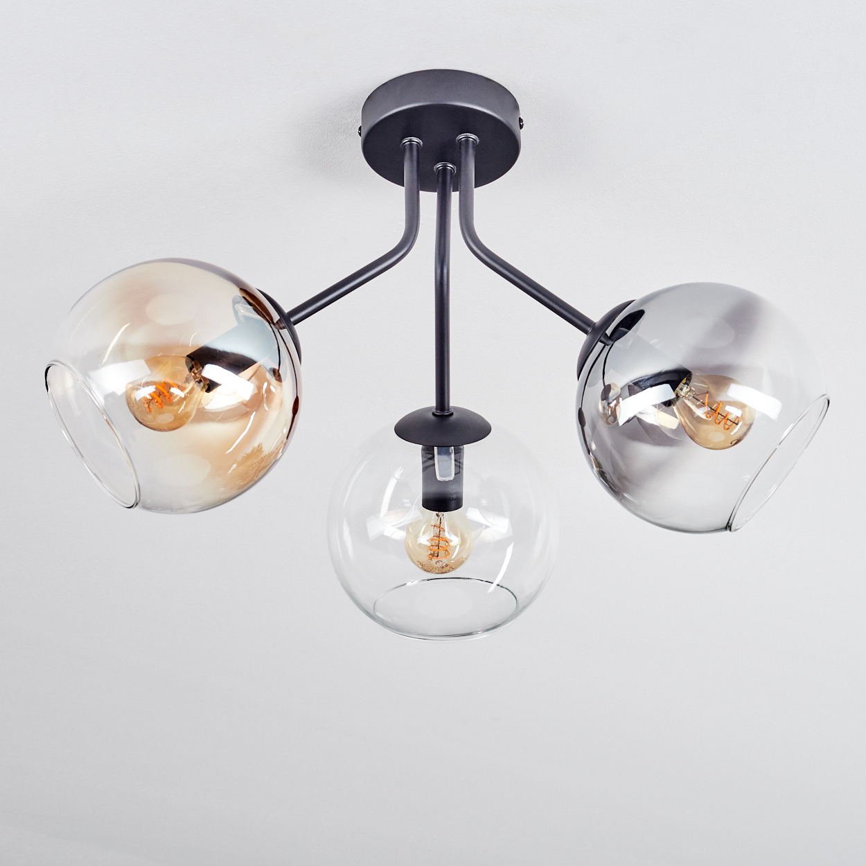 Eine moderne Deckenlampe mit drei kugelförmigen Schirmen. Jeder enthält eine Glühbirne. Die Schirme sind klar und getönt. Die Halterung ist schwarz.