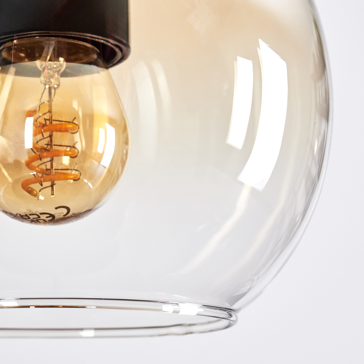 Nahaufnahme einer Glühbirne in einer Glaskugel. Der Glühfaden der Glühbirne ist sichtbar. Das Glas hat eine reflektierende Oberfläche.