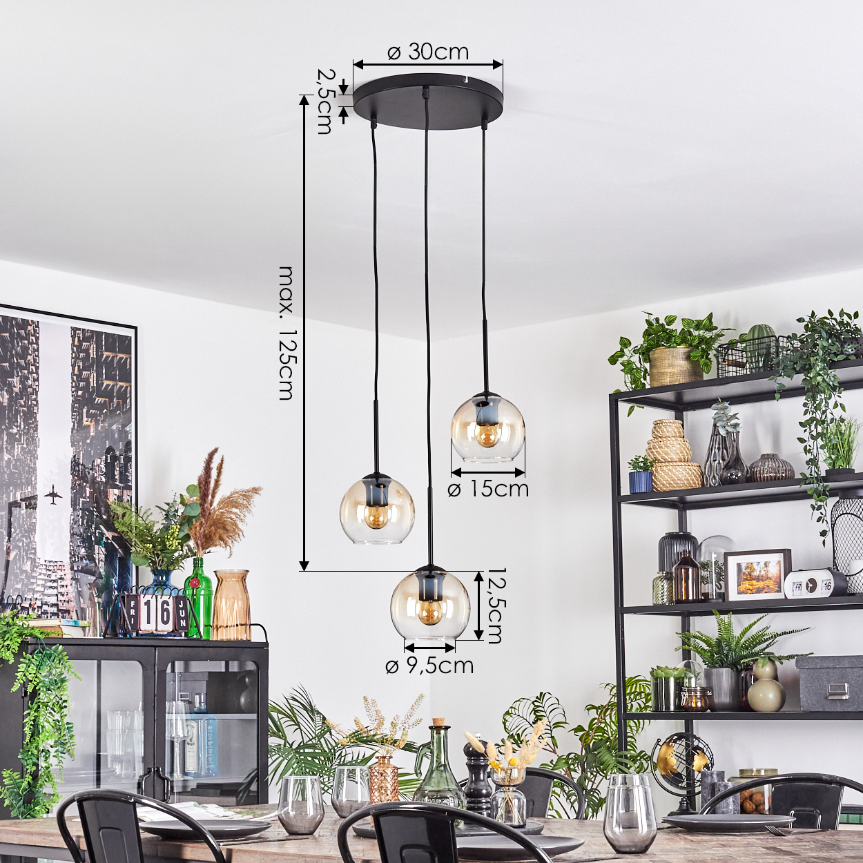 Drei Pendelleuchten mit Glaskugeln hängen über einem Holztisch. Im Hintergrund ein schwarzes Metallregal mit Pflanzen.