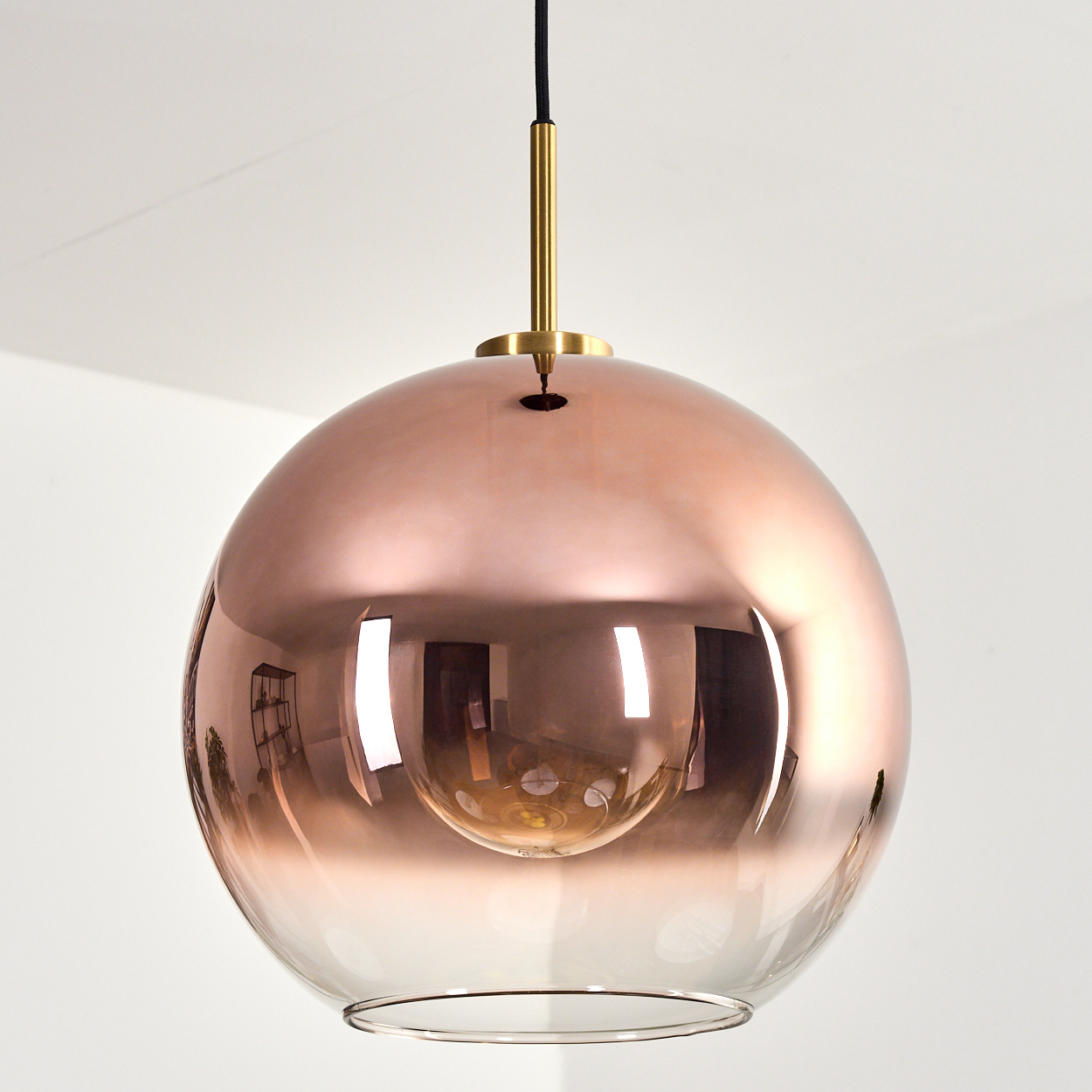 Eine moderne Pendelleuchte mit kupferfarbenem, kugelförmigem Schirm. Der untere Teil des Schirms ist transparent. Sie hängt von der Decke.