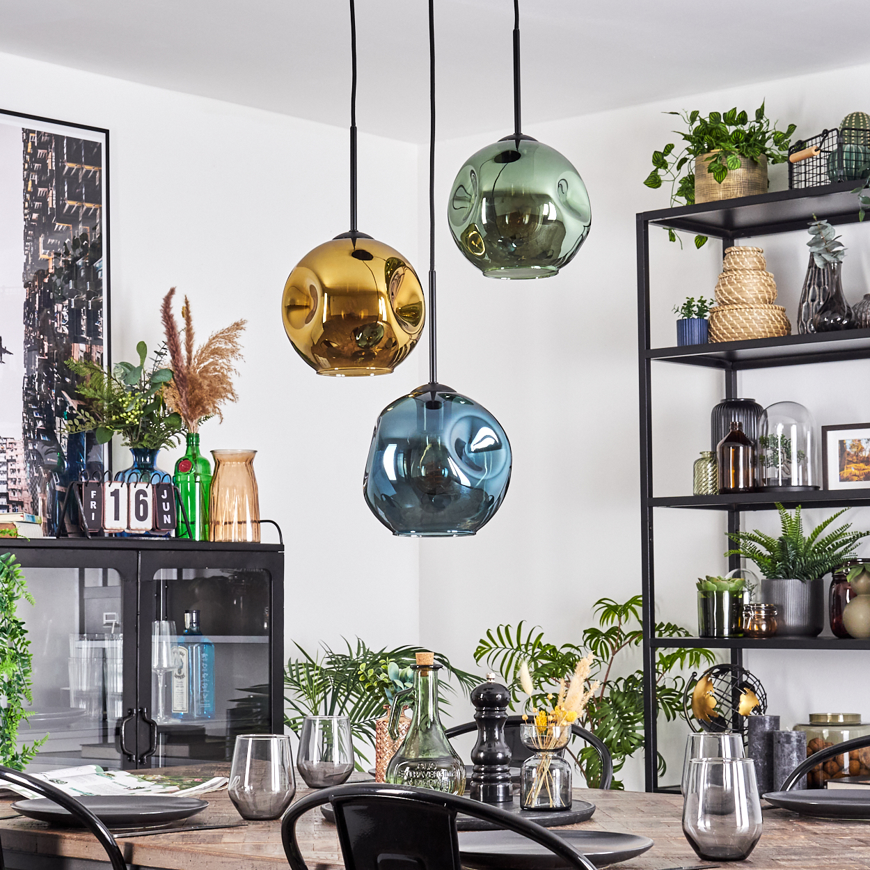 Esszimmer mit drei Hängelampen und einem gedeckten Tisch. Regale mit Dekoration befinden sich im Hintergrund.