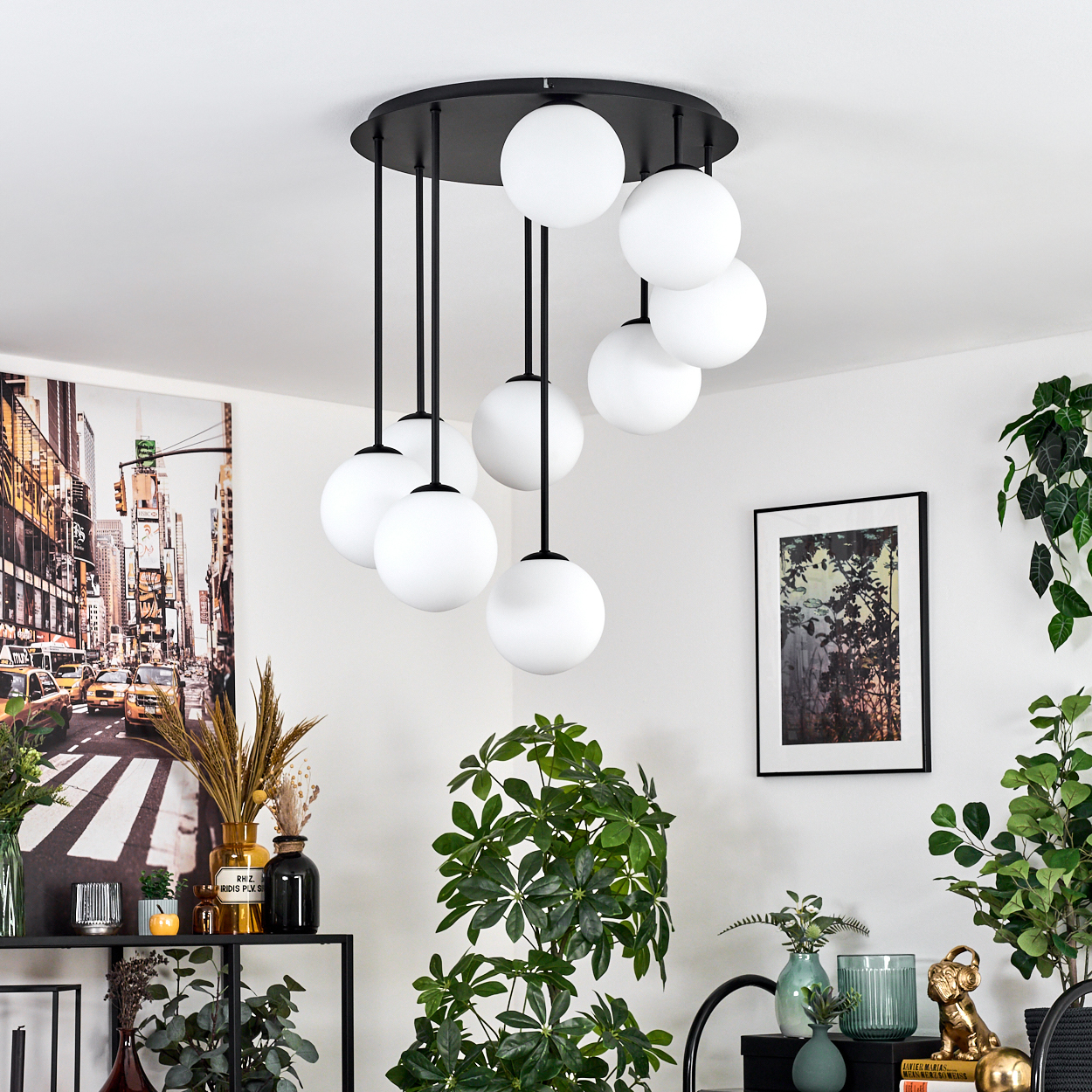 Ein modernes Wohnzimmer mit einem schwarzen Kronleuchter mit weißen Kugeln, einem Stadtbild-Kunstdruck und verschiedenen Pflanzen.