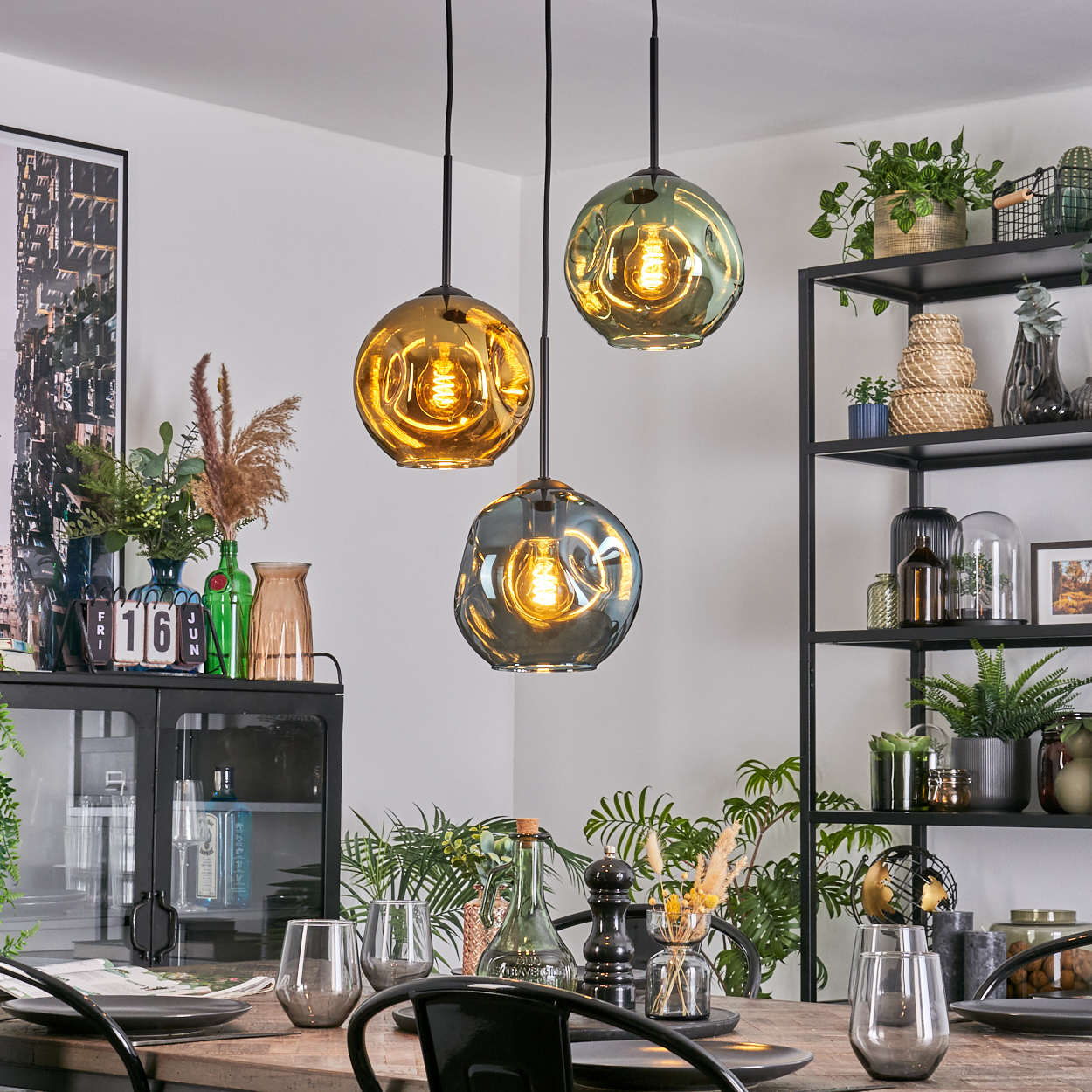 Esszimmer mit drei Hängelampen. Tisch mit Gläsern und Tellern gedeckt. Regale mit Pflanzen und Dekoration.