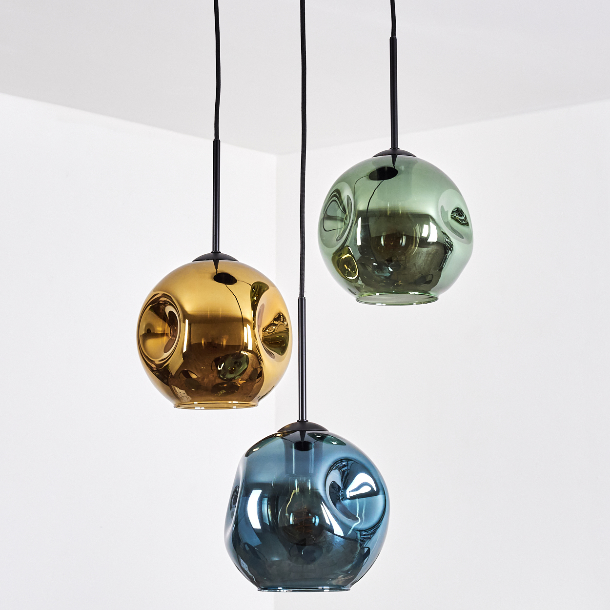Drei blasenartige Pendelleuchten, gold, grün und blau, hängen an schwarzen Schnüren vor weißem Hintergrund.