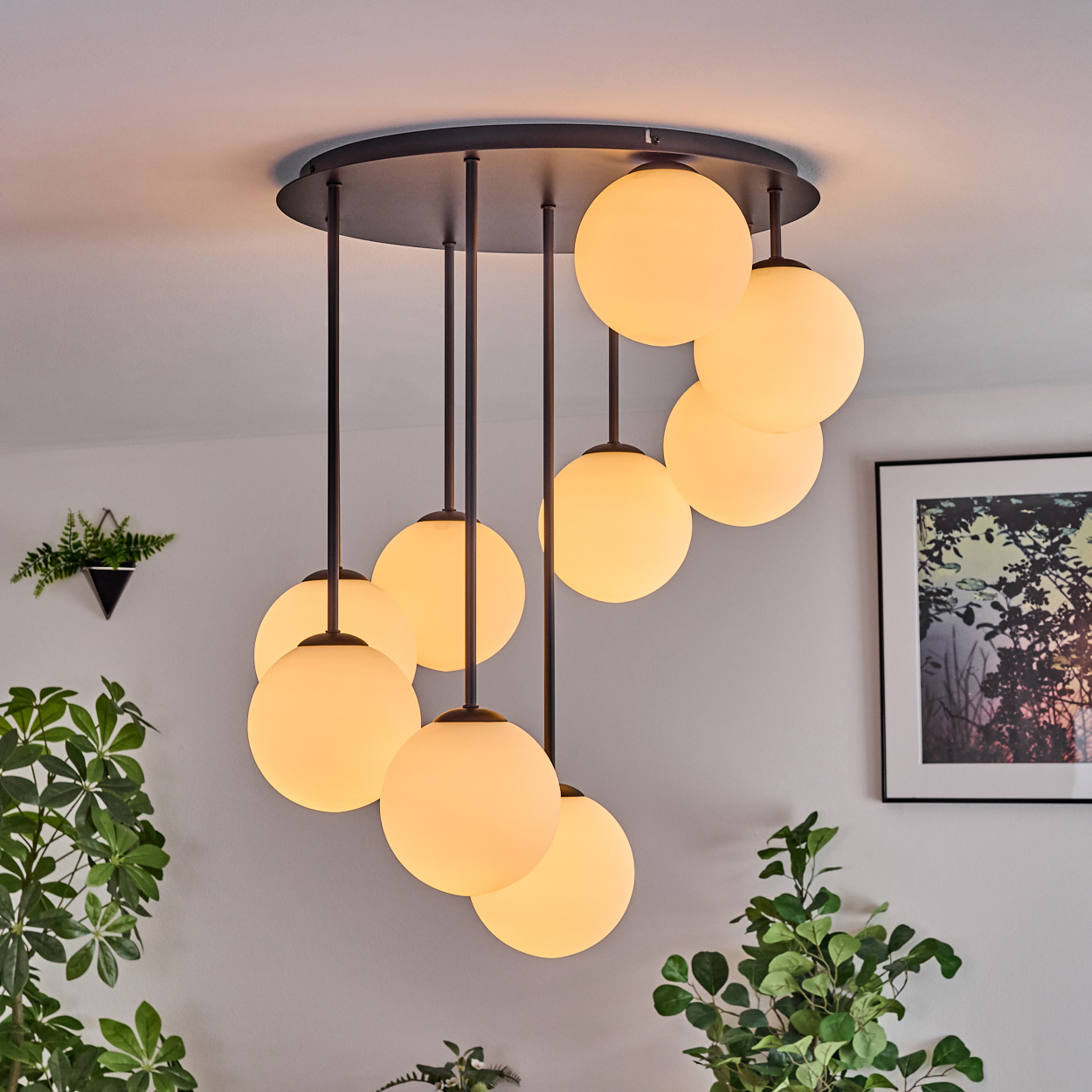 Eine moderne Deckenleuchte mit kugelförmigen Lichtern hängt von der Decke. Pflanzen und gerahmte Kunstwerke sind ebenfalls im Raum zu sehen.