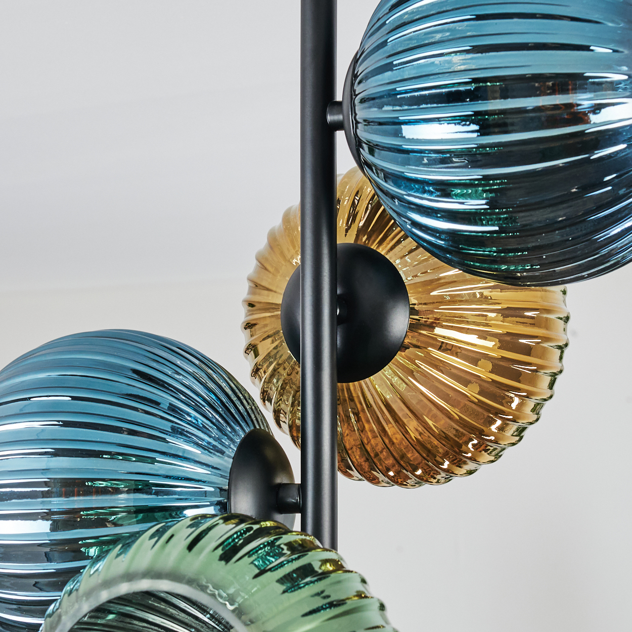 Nahaufnahme einer modernen Lampe mit vier gerippten Glaskugeln in Blau, Gold und Grün. Schwarzes Metall stützt die Kugeln.