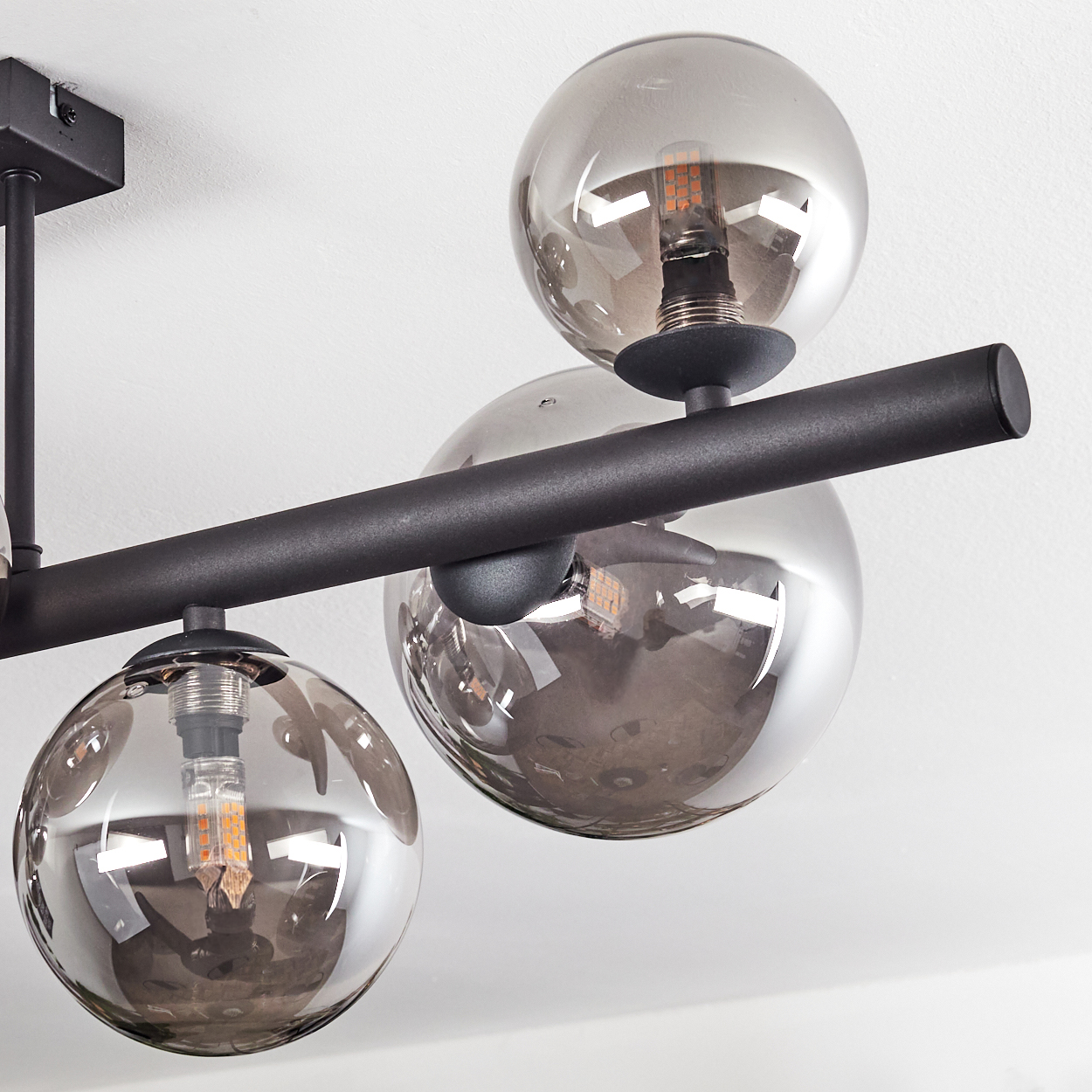 Eine moderne schwarze Pendelleuchte mit drei kugelförmigen, rauchigen Glasschirmen, jede mit einer freiliegenden Glühbirne. Der Hintergrund ist weiß.