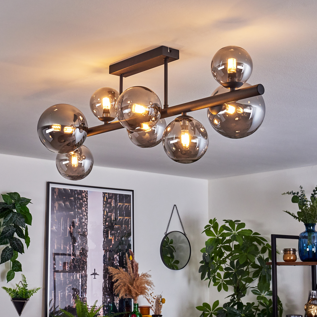 Eine moderne Deckenleuchte mit Glaskugeln beleuchtet den Raum. Pflanzen und ein Bildrahmen sind im Hintergrund zu sehen.