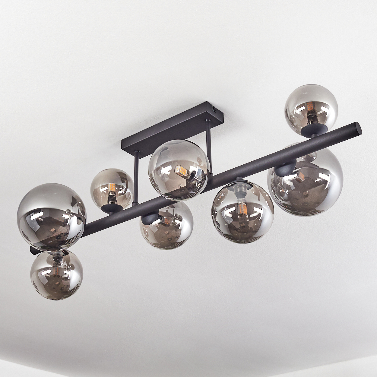 Moderne Deckenleuchte mit acht rauchfarbenen Glaskugeln. Sie ist an einem schwarzen Metallrahmen an einer weißen Decke befestigt.