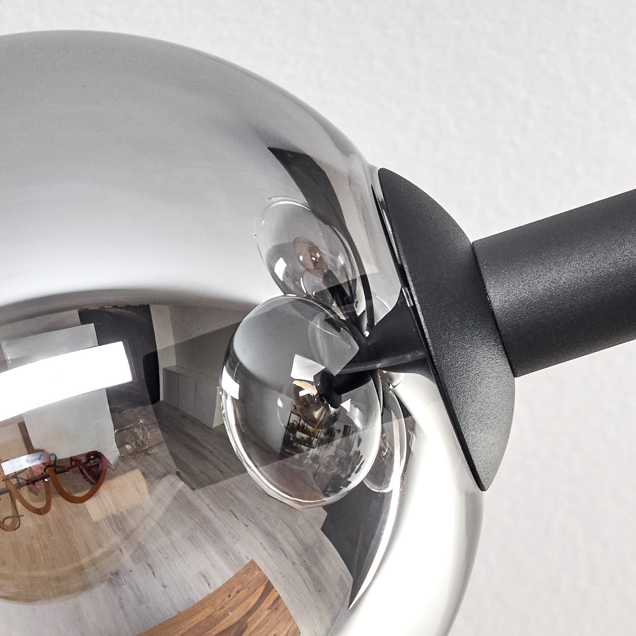 Nahaufnahme einer modernen Lampe. Sie hat eine Chromkugel mit kleineren Glaskugeln und einen schwarzen Arm. Die Reflexion zeigt einen Raum.