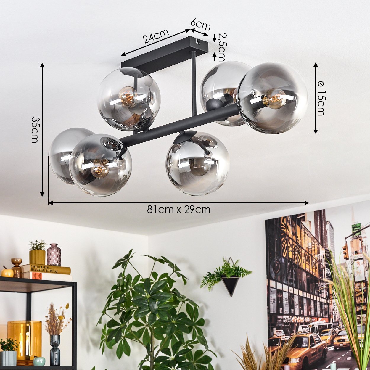 Eine moderne Deckenlampe mit sechs kugelförmigen Schirmen. Abmessungen sind angegeben. Eine Pflanze und Kunstwerk sind im Hintergrund.