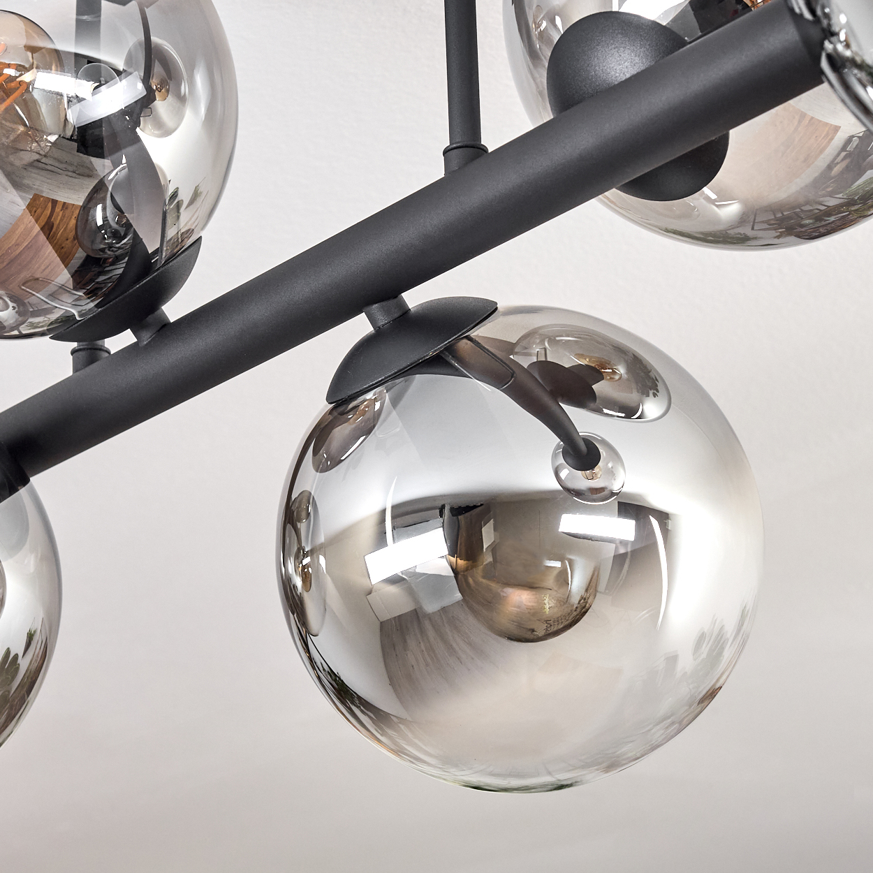 Ein moderner Kronleuchter mit mehreren kugelförmigen Glasschirmen. Schwarze Metallarme tragen die Schirme vor weißem Hintergrund.