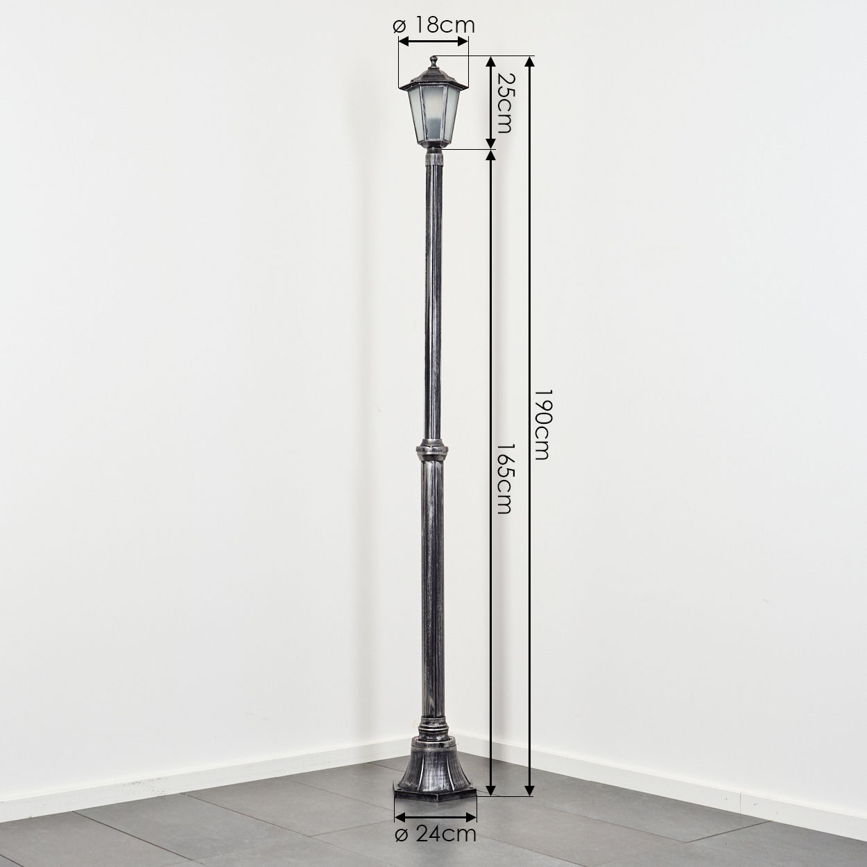 Eine dekorative Außenlaterne. Sie ist dunkelgrau mit angegebenen Abmessungen. Sie steht auf grauen Fliesen vor einer weißen Wand.