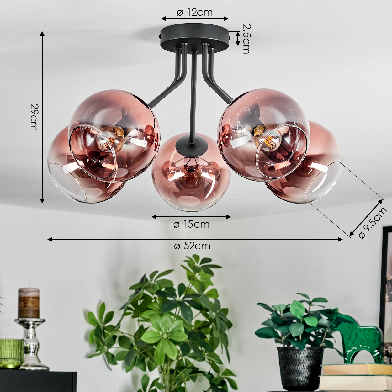 Deckenlampe mit fünf rosa Glaskugeln, schwarzem Rahmen und angegebenen Abmessungen. Grüne Pflanzen und andere Dekorationen im Vordergrund.