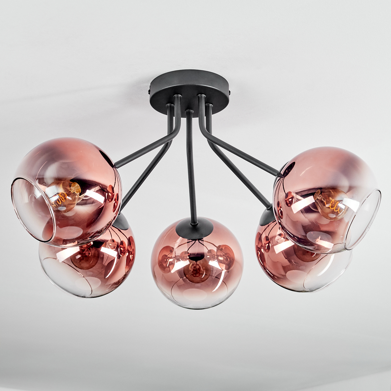 Eine moderne Deckenlampe mit fünf roségoldenen Glaskugeln, jede mit einer sichtbaren Glühbirne, verbunden mit einem schwarzen Metallrahmen.