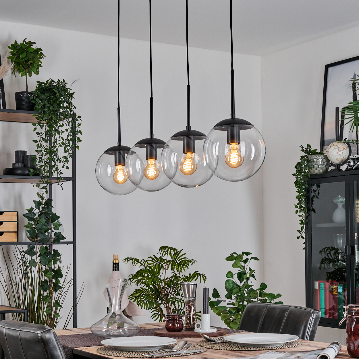 Esszimmer mit vier kugelförmigen Pendelleuchten. Pflanzen, Holztisch, Teller und eine Weinkaraffe sind sichtbar.