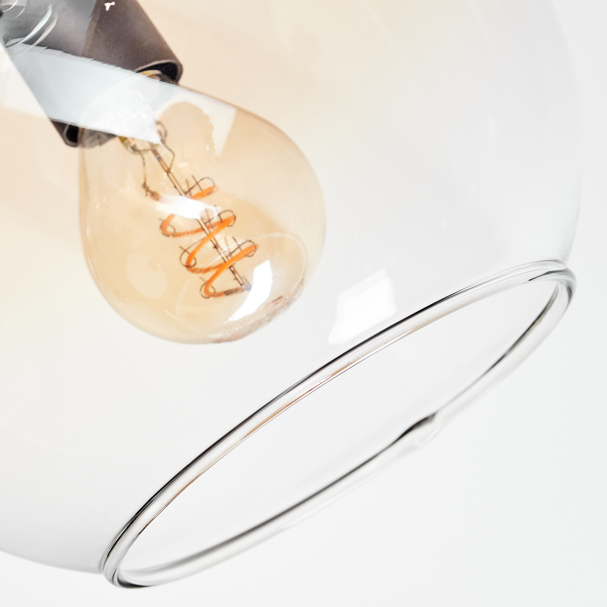 Nahaufnahme einer Leuchte mit klarem Glasschirm. Im Inneren ist eine Glühbirne mit warmem, orangefarbenem Glühen und einer gewendelten Glühwendel zu sehen.