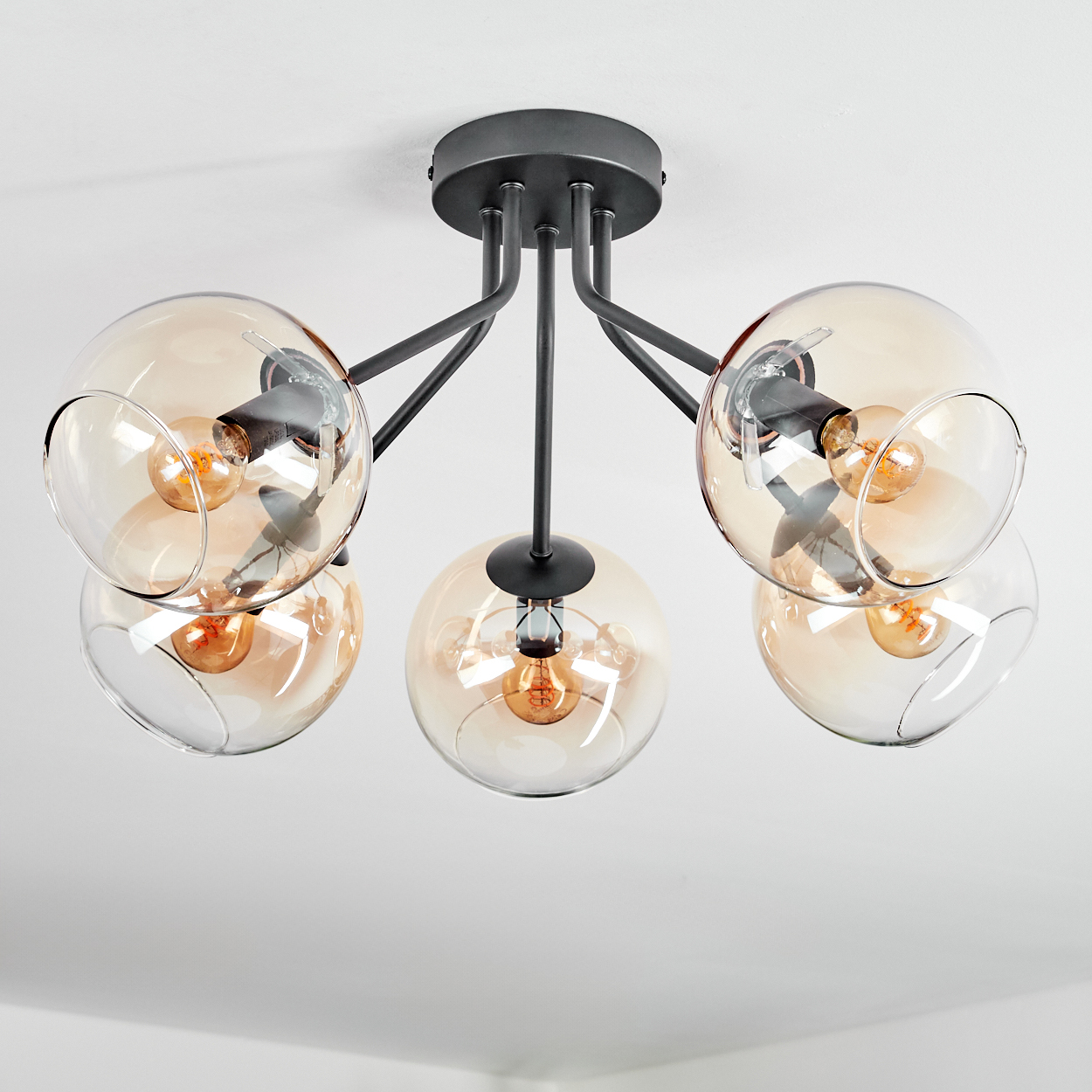 Moderne Deckenleuchte mit fünf bernsteinfarbenen Glaskugelschirmen, schwarzen Metallarmen und freiliegenden Glühbirnen, an der Decke.