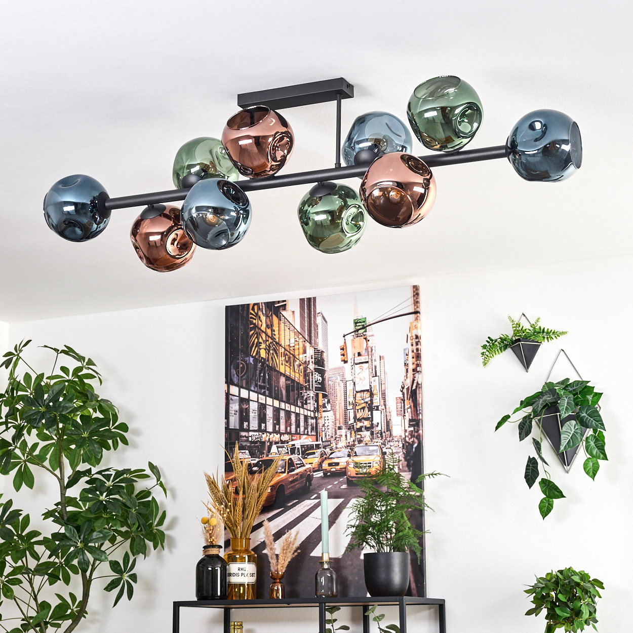 Eine moderne Deckenleuchte mit farbigen Glaskugeln hängt über einem Regal mit Pflanzen und einem Gemälde der New Yorker Skyline.