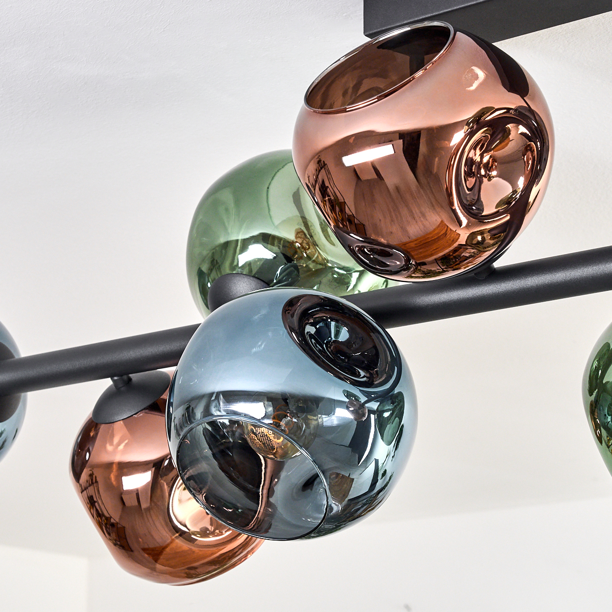Eine moderne Deckenleuchte mit mehreren kugelförmigen Glasschirmen in Kupfer, Grün und Blau, montiert auf einem schwarzen Metallrahmen.
