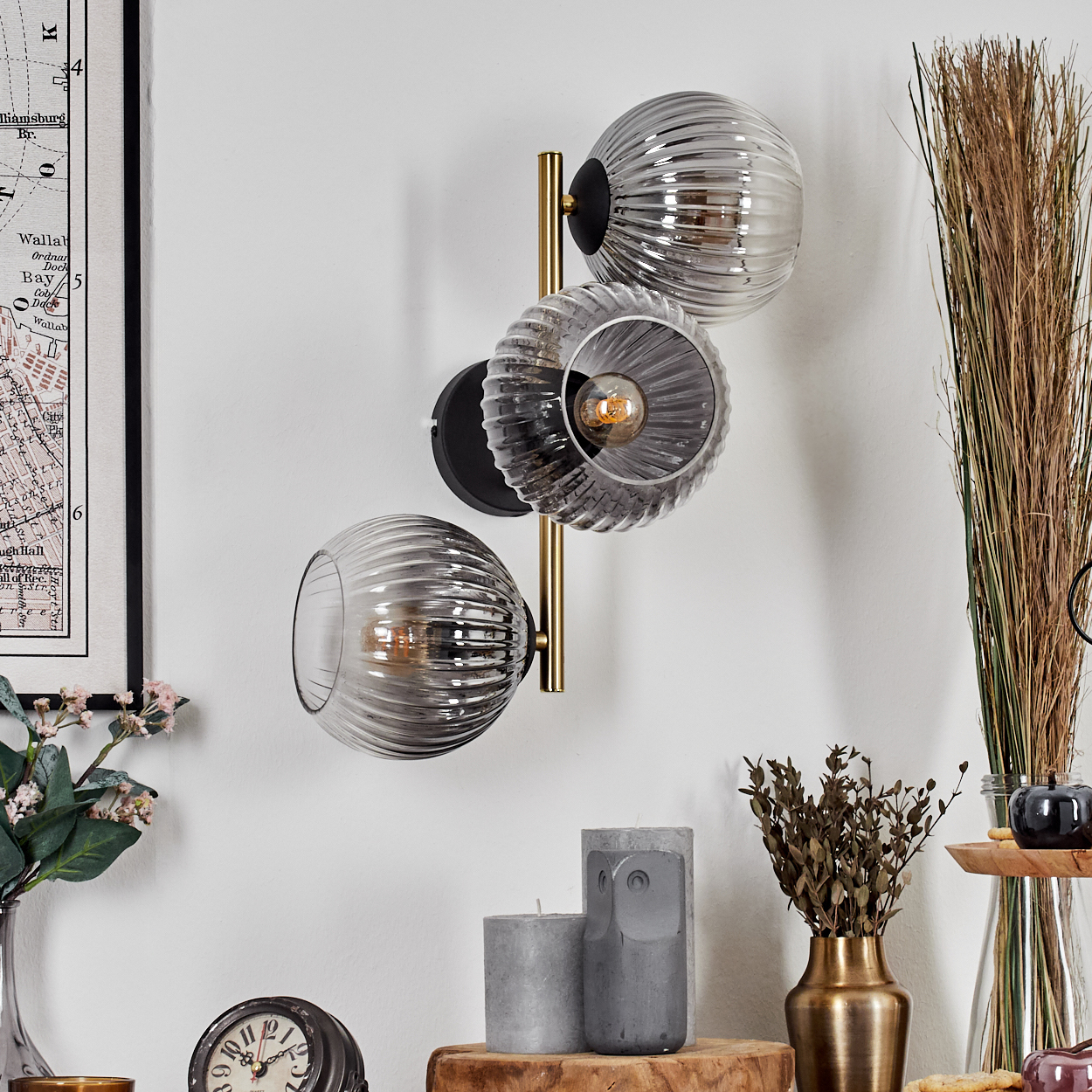 Eine Wandlampe mit drei Glaskugeln. Im Hintergrund eine Uhr, Kerzen und eine Karte.