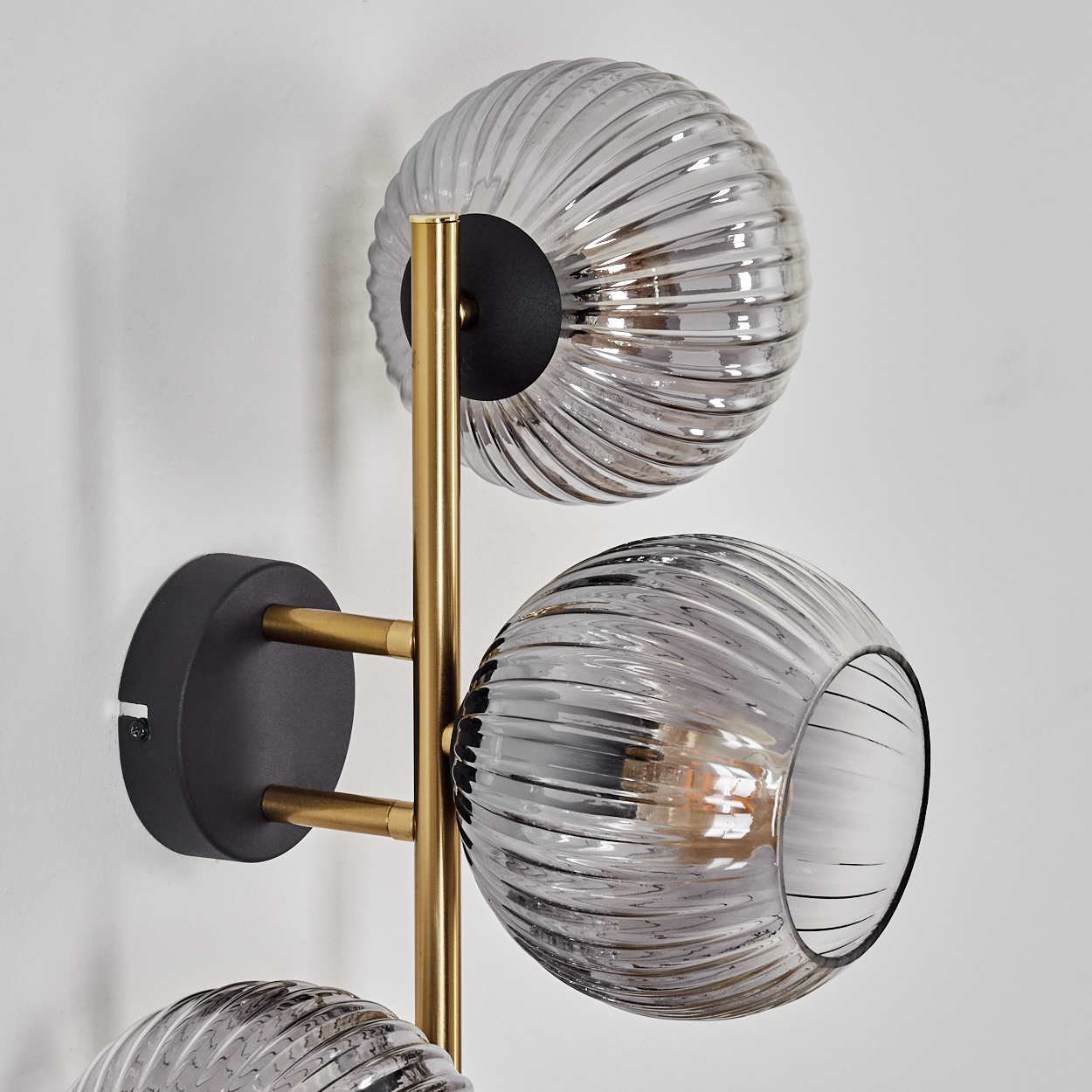 Eine moderne Wandlampe mit drei Glaskugeln. Die Kugeln sind grau, an einem goldenen Rahmen befestigt und an einer weißen Wand montiert.