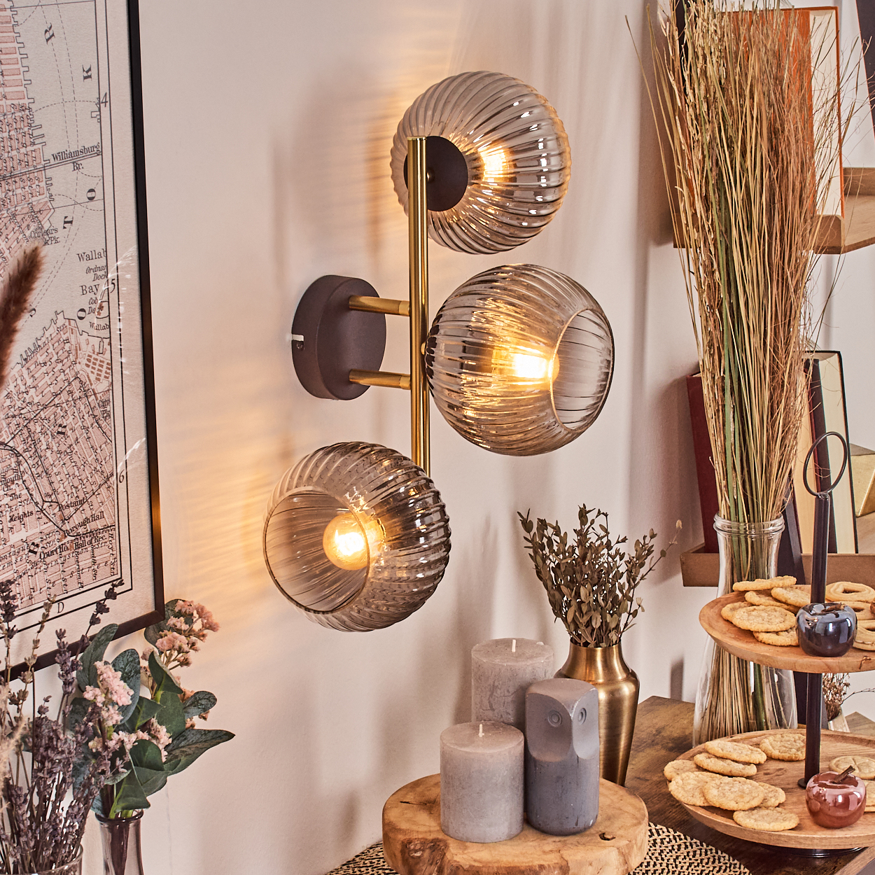Eine Wandlampe mit drei Glaskugeln. Kerzen, Kekse und andere Dekorationen stehen auf einem Holztisch. Links ist eine Karte.